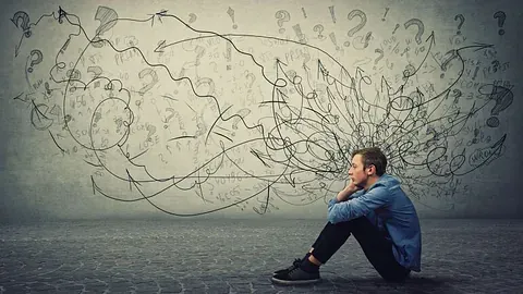 Mann sitter på bakken omgitt av kaotiske tanker og spørsmålstegn.