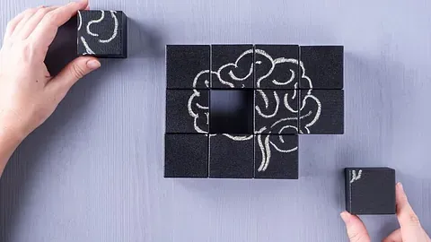 Hender legger svarte klosser med tegning av en hjerne på et bord.