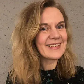 Kvinne med langt blondt hår smiler foran grå bakgrunn.